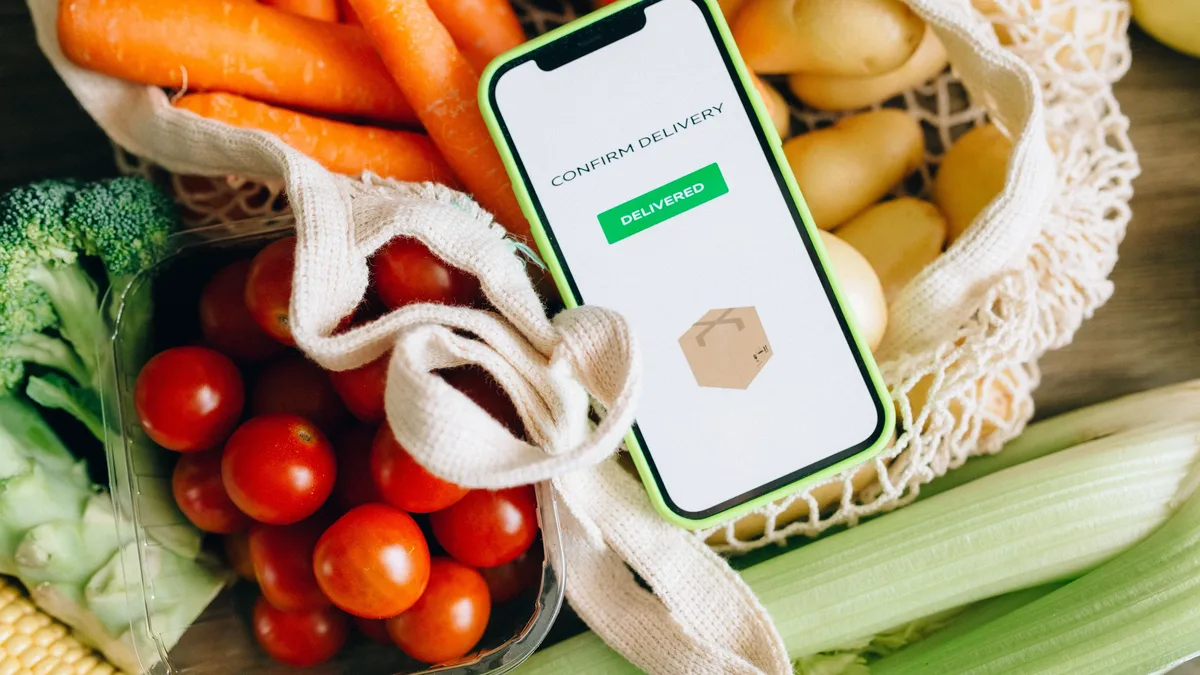 A smartphone with a grocery delivery app on its screen, placed on top of a collection of fresh vegetables.